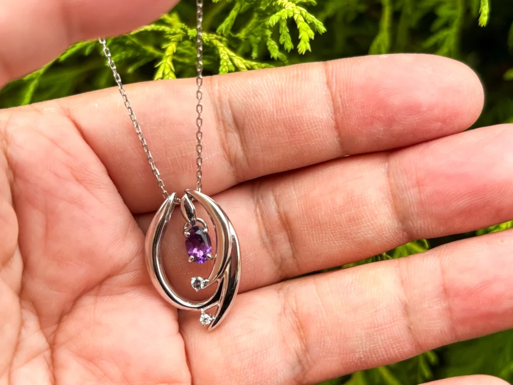 太陽光のもとでROSWAYさんのアメシストのネックレスを手のひらに載せて撮りました。アメシストの色が夜に比べると明るく澄んでいます。植え込みの葉っぱをバックに撮っているので緑と紫の対比が鮮やかです。